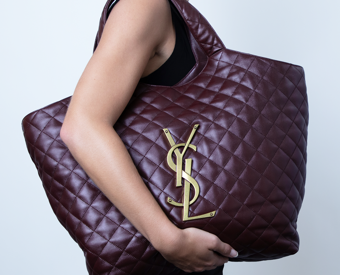 Woman holding a large dark purple YSL handbag over her shoulder