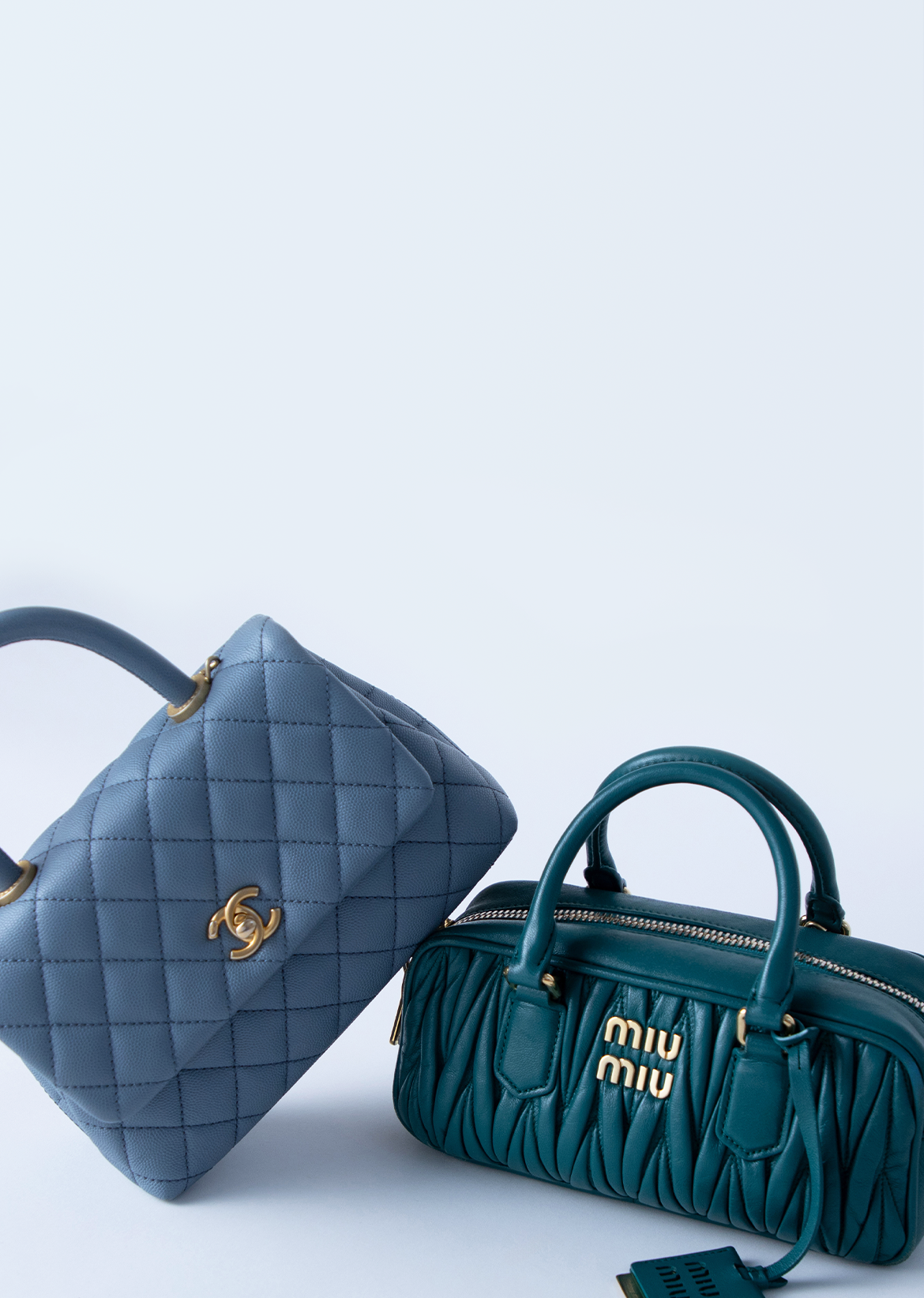 Light blue Chanel handbag leaning against a teal Miu Miu handbag against a sky blue background